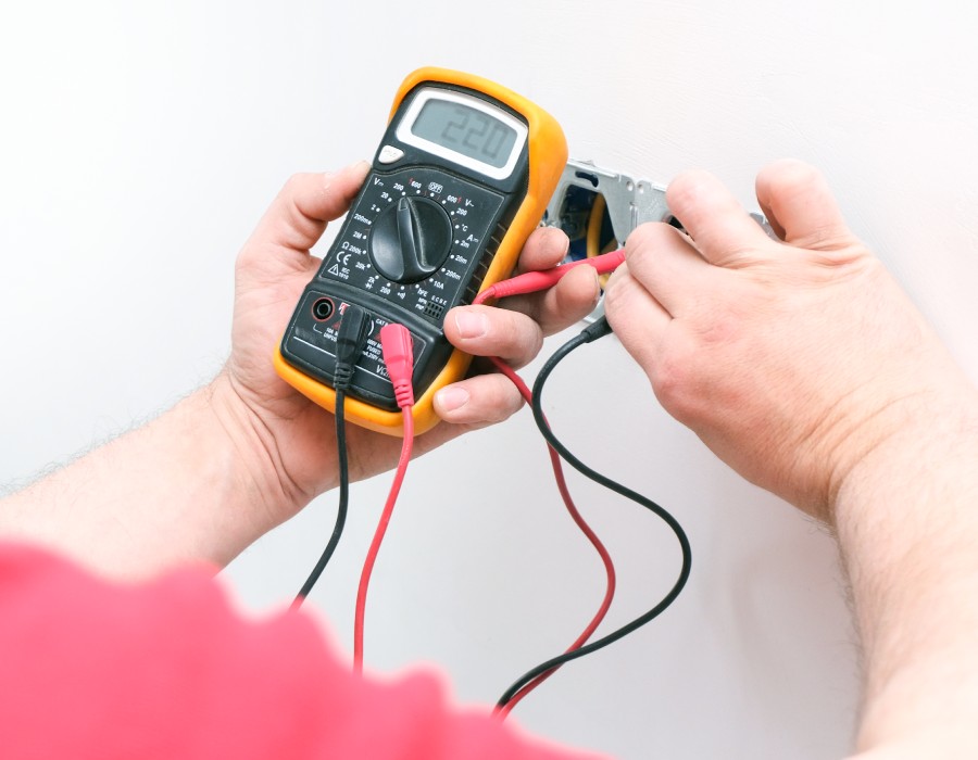Électricien mesurant la tension d’une prise murale avec un multimètre